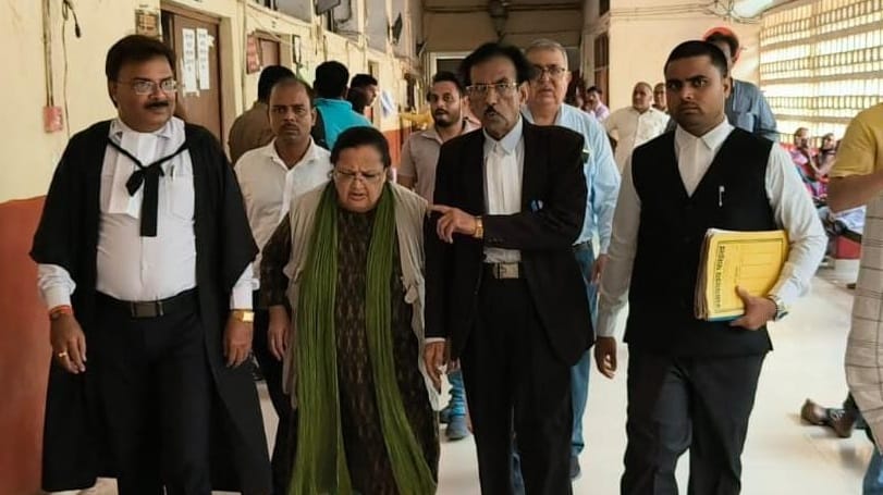 A group of formally dressed people walking down a hallway, led by a woman in green scarf, flanked by men in suits.